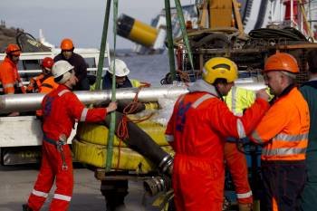 Trabajadores cargan tubos y otros materiales que serán empleados en las labores de extracción del combustible del depósito del crucero 'Costa Concordia', semihundido en la costa de la isla italiana de Giglio (Foto: EFE)