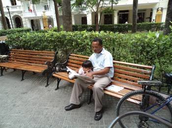 Un hombre lee un libro con su pequeño hijo, sentados en un banco en el parque. (Foto: ARCHIVO)