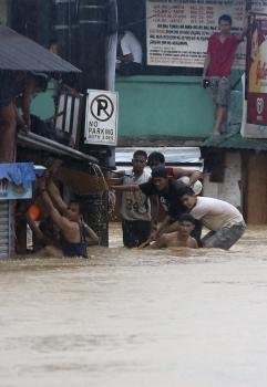 Varias personas intentan resguardarse de la lluvia en una calle inundada por un monzón temporal