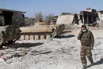 Un soldado habla por el móvil rodeado de tanques y ruinas, en un suburbio de Damasco. (Foto: EFE)