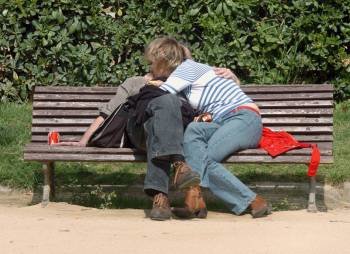 Dos jóvenes se abrazan en el banco de un parque.