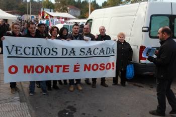 Parte de los manifestantes exhiben la pancarta en el centro de Vilavidal. Al fondo, los puestos ambulantes de la feria.  (Foto: JOSE PAZ)