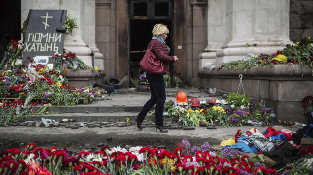 Una mujer pasa junto a las ofrendas florales por la muerte el pasado viernes de 46 personas en la Cámara de Comercio de la ciudad de Odessa