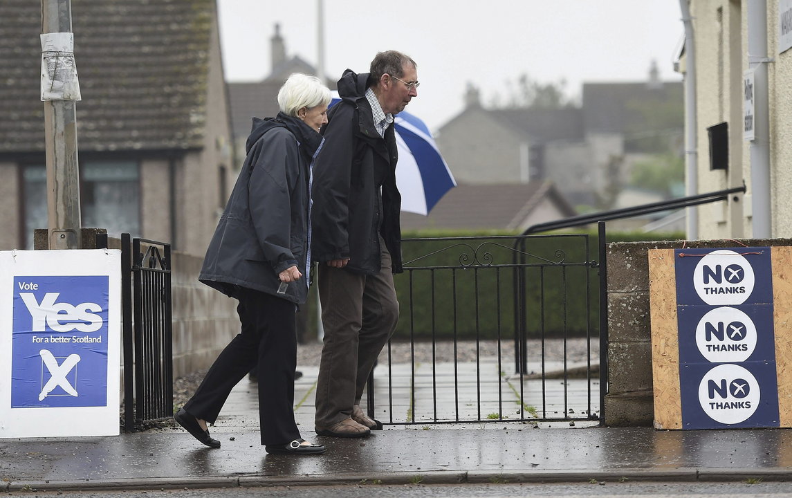 Una pareja pasa delante de una pancarta a favor del &#34;sí&#34; (i) y otra del &#34;no&#34; (d) a la independencia de Escocia del Reino Unido tras votar en un colegio electoral 
