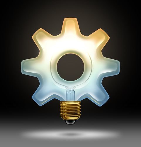 Business innovation and creativity as a lightbulb illuminated glass in the shape of a gear or cog as a concept of creative success in innovative ideas for industry and bright thinking on a black background.