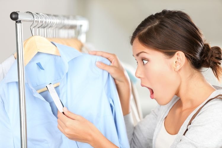 Shopping woman shocked over price tag. Funny shopper woman staring amazed at price. Mixed race Caucasian / Asian Chinese young female model in clothing shop.