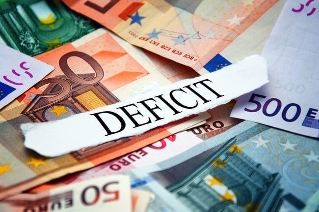 Word "Deficit" printed on a piece of paper and placed above the pile of euro banknotes