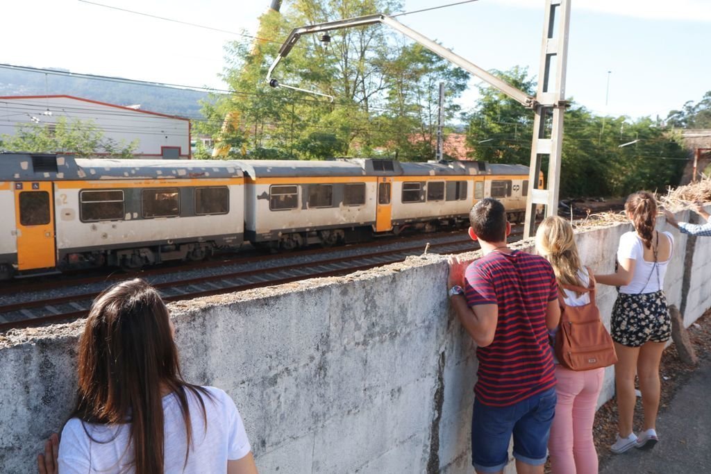 Un tren pasa ayer por el lugar del accidente con los  restos del convoy,  ante la mirada de  vecinos de Porriño.