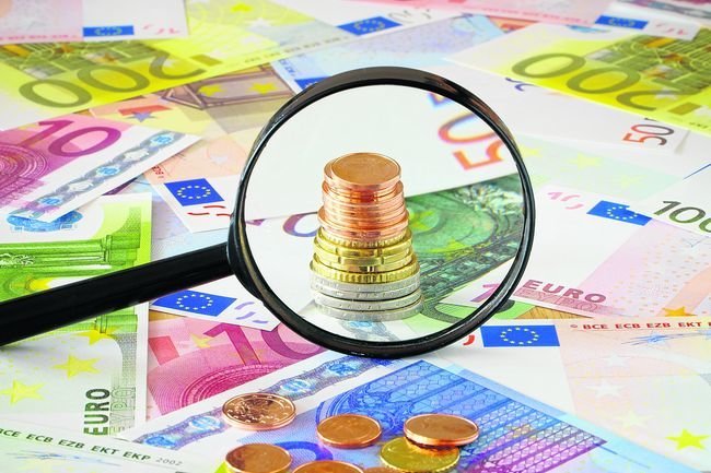 Coin stack behind magnifying glass on a background made of Euro banknotes and coins