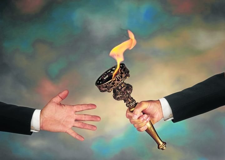 Businessman's outstretched arm passing a flaming torch to another businessman's open hand