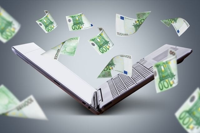 Finance and earning concept, one hundred euro banknotes flying around laptop, internet, side view on dark background.