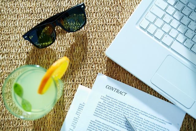 Image of business contract with pen, laptop, cocktail and sunglasses near by