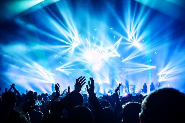 Large group of happy people enjoying rock concert, clapping with raised up hands, blue lights from the stage, new year celebration concept