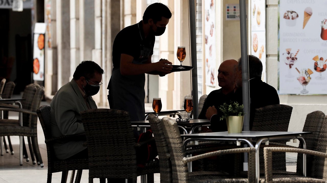 Un camarero sirve unas consumiciones a los clientes en la terraza de un bar. 