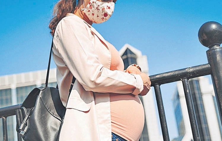 Una mujer embarazada pasea por la calle con la mascarilla puesta.