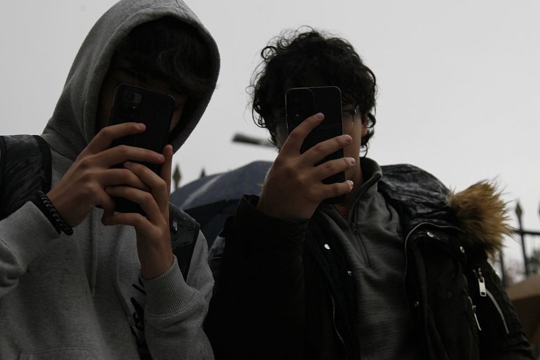 Dos estudiantes con sus teléfonos.