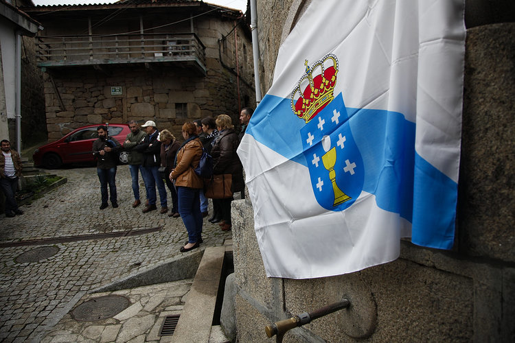Políticos locales y vecinos, junto a la fuente, tapada con la bandera gallega.