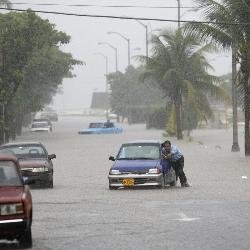 Un hombre trata de empujar su coche en una calle inundada.