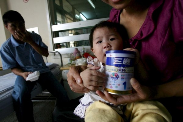 Una madre sostiene a su bebé mientras muestra un bote con polvos de leche de la marca Sanlu. (Foto: D.Wong)