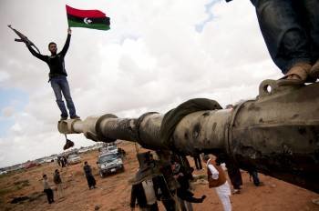 Un miliciano insurgente ondea la bandera de Libia subido encima de los restos de un carro blindado de las fuerzas de Gadafi. (Foto: MANU BRABO)
