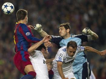 El portero del Real Madrid Iker Casillas (d) despeja el balón ante el defensa del F.C. Barcelona Gerard Piqué
