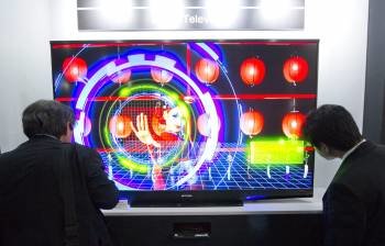 Empresarios japoneses se detienen ante un televisor de la marca Mitsubishi Corp que se caracteriza por tener retroiluminación o luz de fondo Láser, durante la inauguración de la feria de tecnología CEATEC (Foto: EFE)