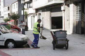 Un barrendero realiza su trabajo junto a vehículos estacionados, en la avenida del Balneario. (Foto: XESÚS FARIÑAS)