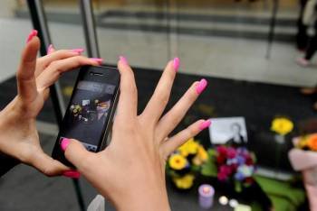 Un mujer utiliza su iPhone para tomar una foto de varios ramos de flores depositados a las puertas de una tienda de Apple en Sídney (Australia), tras conocerse la muerte de Steve Jobs. Foto: Tracey Nearmy