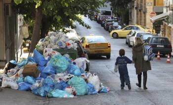 Una madre y su hijo pasan junto a un montón de bolsas de basura apiladas en una calle de Atenas (Grecia) (Foto: EFE)