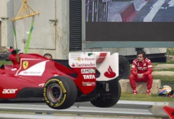Fernando Alonso observa sentado en el suelo como una grúa se lleva su monoplaza tras su avería. (Foto: DIEGO AZUBEL)