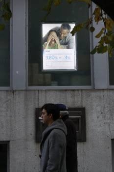 Dos `personas pasan ante un anuncio de planes de pensiones (Foto: XESÚS FARIÑAS)