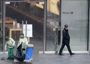Un policía observa a trabajadores que limpian en el exterior de una tienda Apple después de una pelea entre un grupo de personas que espera comprar el nuevo iPhone 4S (Foto: EFE)