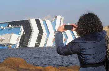 Una mujer fotografía hoy, domingo 15 de enero de 2012, desde la isla de Giglio (Italia), el crucero 'Costa Concordia', que naufragó el pasado 13 de enero (Foto: EFE)