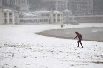Un hombre sale del agua hoy en la playa de La Concha de San Sebastián, donde la nieve ha empezado a cuajar a nivel del mar