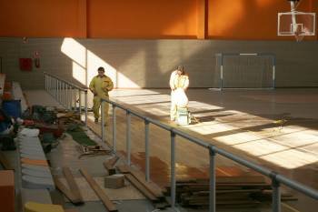 Dos operarios adecentan el piso de madera en el interior del pabellón deportivo. (Foto: MARCOS ATRIO)