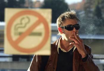 Un hombre apura un cigarrillo en el exterior de un local con un cartel de prohibido fumar.