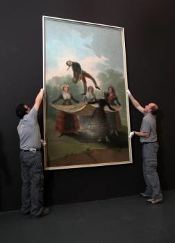 Operarios cuelgan de la pared el cuadro de Francisco de Coya 'El pelele', de 1791, durante el montaje de la exposición 'Goya: Luces y Sombras'. Foto: Toni Albir