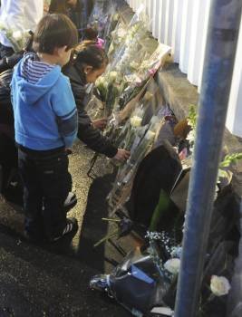 Dos niños depositan flores en la valla del colegio. (Foto: CAROLINE BLUMBERG)