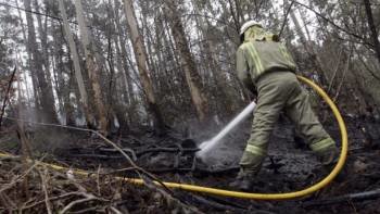 Un miembro de los efectivos contra incendios esparce agua para enfriar la superficie ya quemada. (Foto: ARCHIVO)