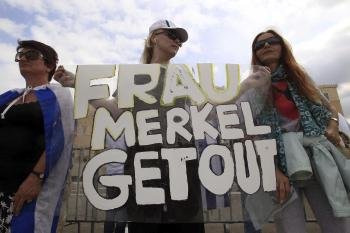 Una manifestante sujeta una pancarta en la que se puede leer 'Frau Merkel Lárgate' durante una protesta frente la sede parlamentaria griega