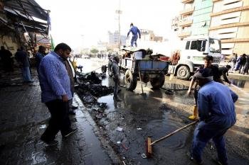 Trabajadores municipales iraquíes limpian el escenario de un ataque con coche bomba en Kerbala, al sur de Irak