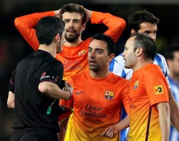 Xavi, encima del árbitro de Anoeta junto a sus compañeros Piqué e Iniesta. (Foto: JUAN HERRERO)