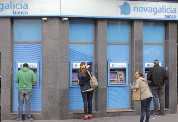 Tres personas hacen uso de los cajeros automáticos de una oficina de Novagalicia en Santiago. (Foto: E.P.)