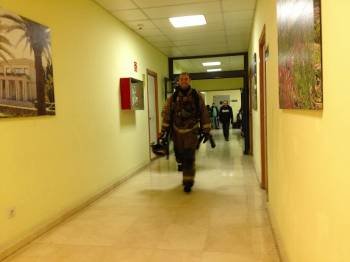 Un bombero sale del Hospital por el pasillo, tras realizar su trabajo. Al fondo, enfermos y familiares.