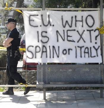 Un policía camina junto a una pancarta en la que se puede leer 'Unión Europea, ¿Quién es el siguiente? España o Italia' frente al Parlamento en Nicosia (Chipre).