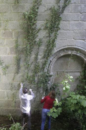 Dos voluntarios limpian la parte posterior del monasterio. (Foto: XESÚS FARIÑAS)