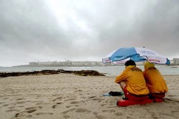 Dos socorristas se protegen de la lluvia en la playa coruñesa de Riazor. (Foto: CABALAR)
