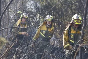 Tres agentes de las brigadas contra incendios caminan entre las ramas calcinadas del monte de Cartelle. A la derecha, un helicópeto cerca de una zona habitada. (Foto: FOTOS: XESÚS FARIÑAS)