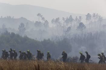 Brigadas del Ministerio de Medio Ambiente pasan ante el humo de un fuego en el monte de Cartelle. (Foto: X. FARIÑAS)