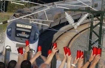 Los vecinos de Angrois alzan los cirios, mientras el conductor los saluda, al paso tren que hace la ruta del que descarriló hace ahora una semana (Foto: efe)